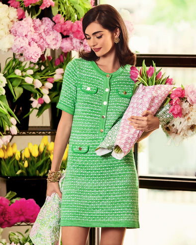 Woman with brown hair in green sweater dress holding flower colorful flower bouquets in front of pink and yellow flowers