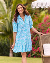 A smiling model outside with flowers in the background in the Jude Connally Tierney Dress - Painted Tile Aqua