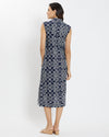 Brunette woman facing away wearing geometric print navy and white rope print midi dress with tan wedge sandals