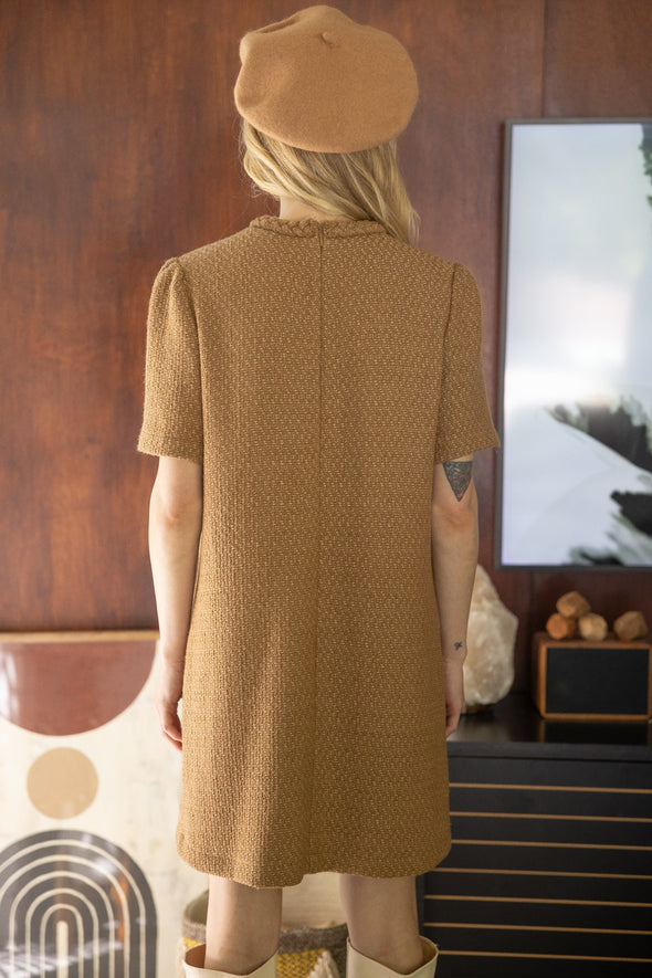 Blonde woman facing away wearing a tan hat and tan camel colored tweed dress