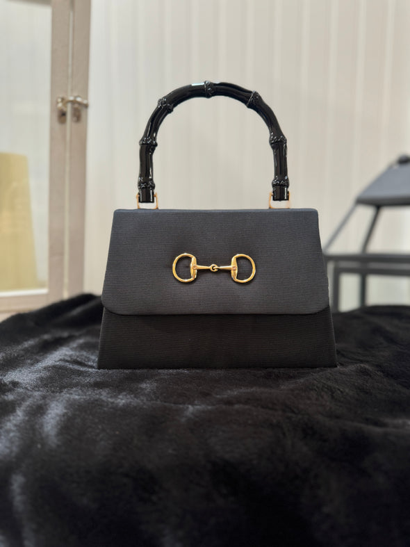 Black faille purse with gold snaffle embellishment on the flap and a black bamboo handle 