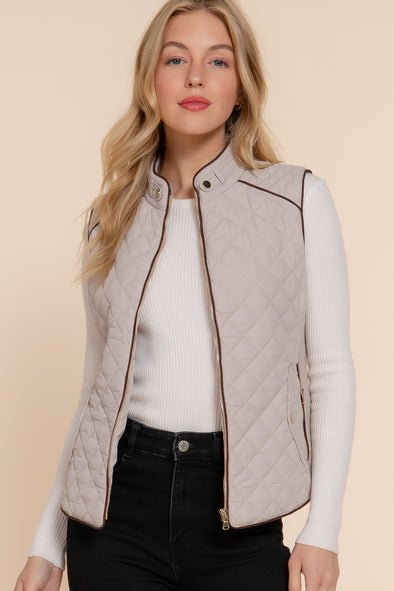 Blonde woman wearing unzipped light taupe vest with brown piping over long sleeve white shirt and dark jeans 