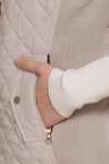 Close up of a hand in a light taupe vest pocket and white long sleeve shirt