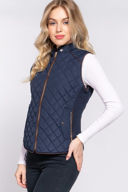 Blonde woman wearing zipped up navy vest over long sleeve white shirt with dark blue jeans 