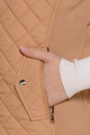 Close up of a hand in a tan vest pocket and white long sleeve shirt